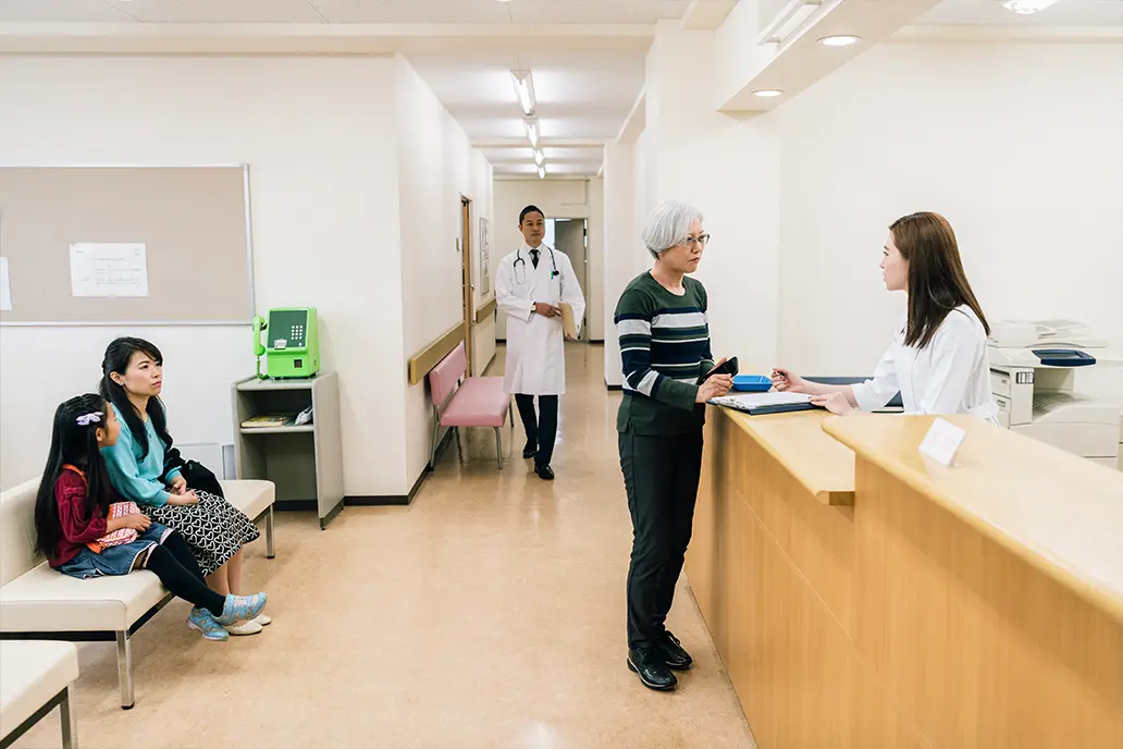 photo of the front reception area of a clinic with patients in the waiting area and a patient checking out with a doctor walking in the background