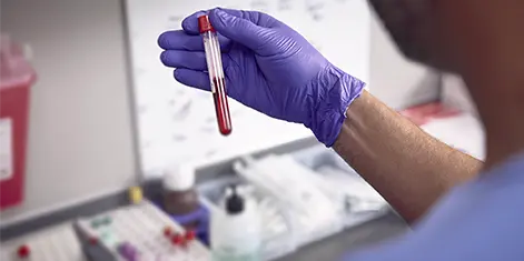 photo of a gloved lab tech examining a test tube filled with a blood sample