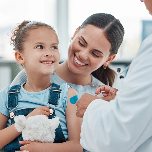 photo of a mother and child in a care setting with a healthcare professional placing an adhesive bandage to child's arm in a clinic