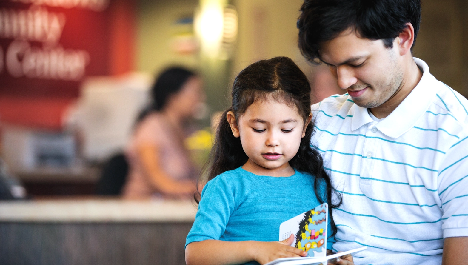photo of a father and daughter waiting for their appointment at a community health center with the reception desk in the background