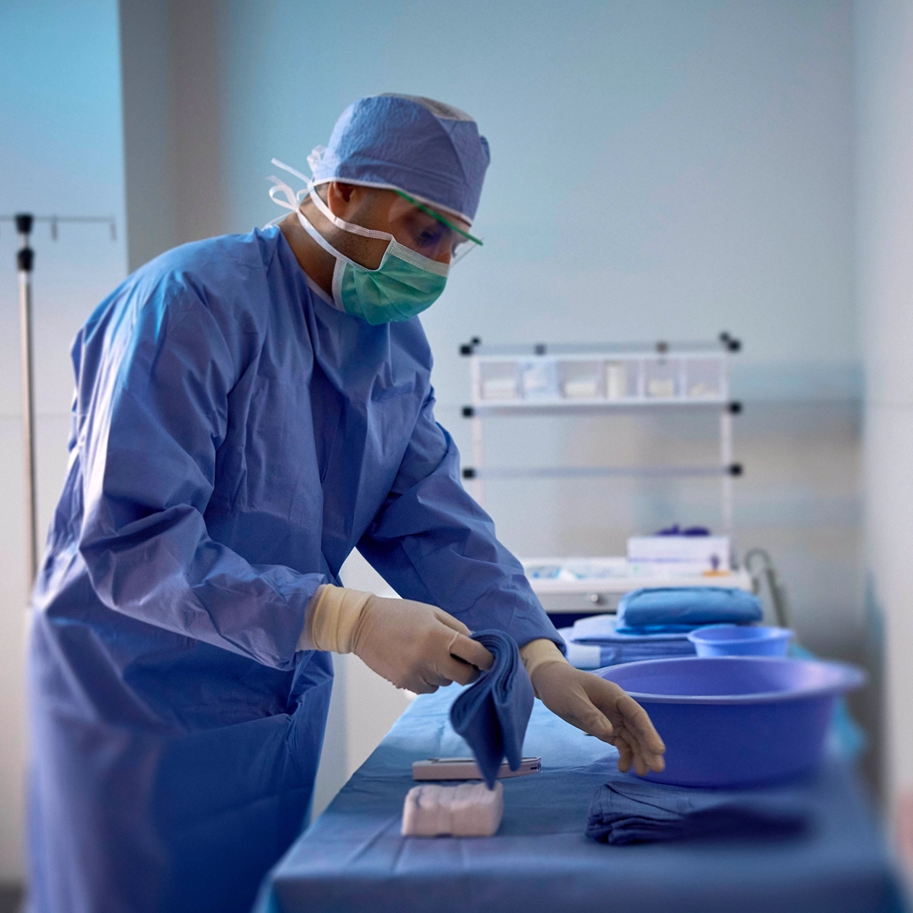 photo of a surgeon donning PPE and preparing a surgical table with supplies