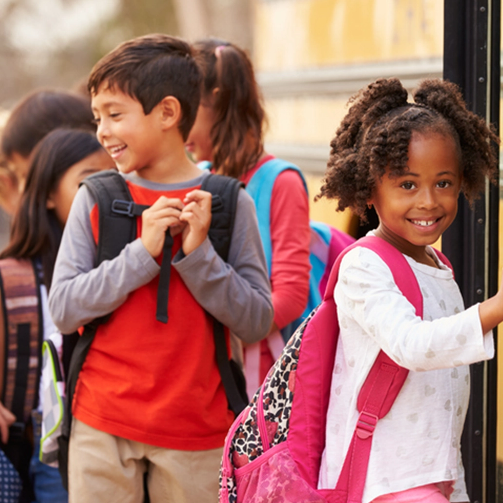 photo of two children smiling as they get on a school bus
