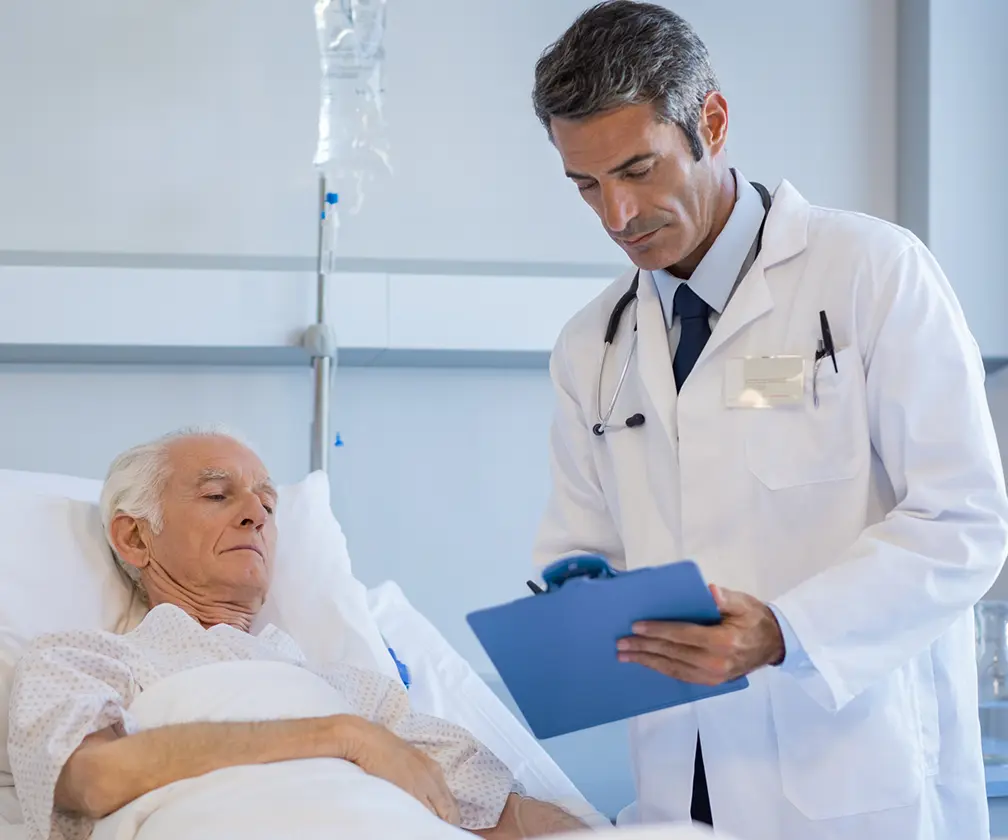 photo of a doctor consulting with an older male patient in a hospital bed with an IV pole in the background