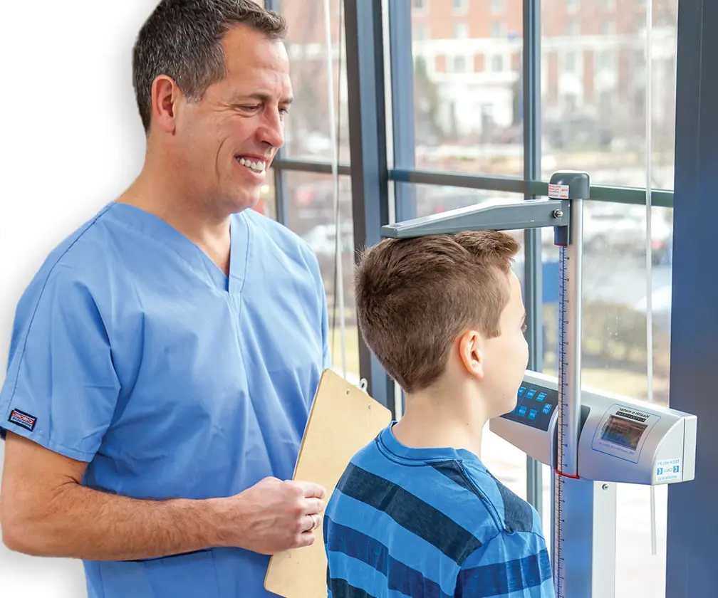 photo of a male nurse using a scale to measure a child patient's height