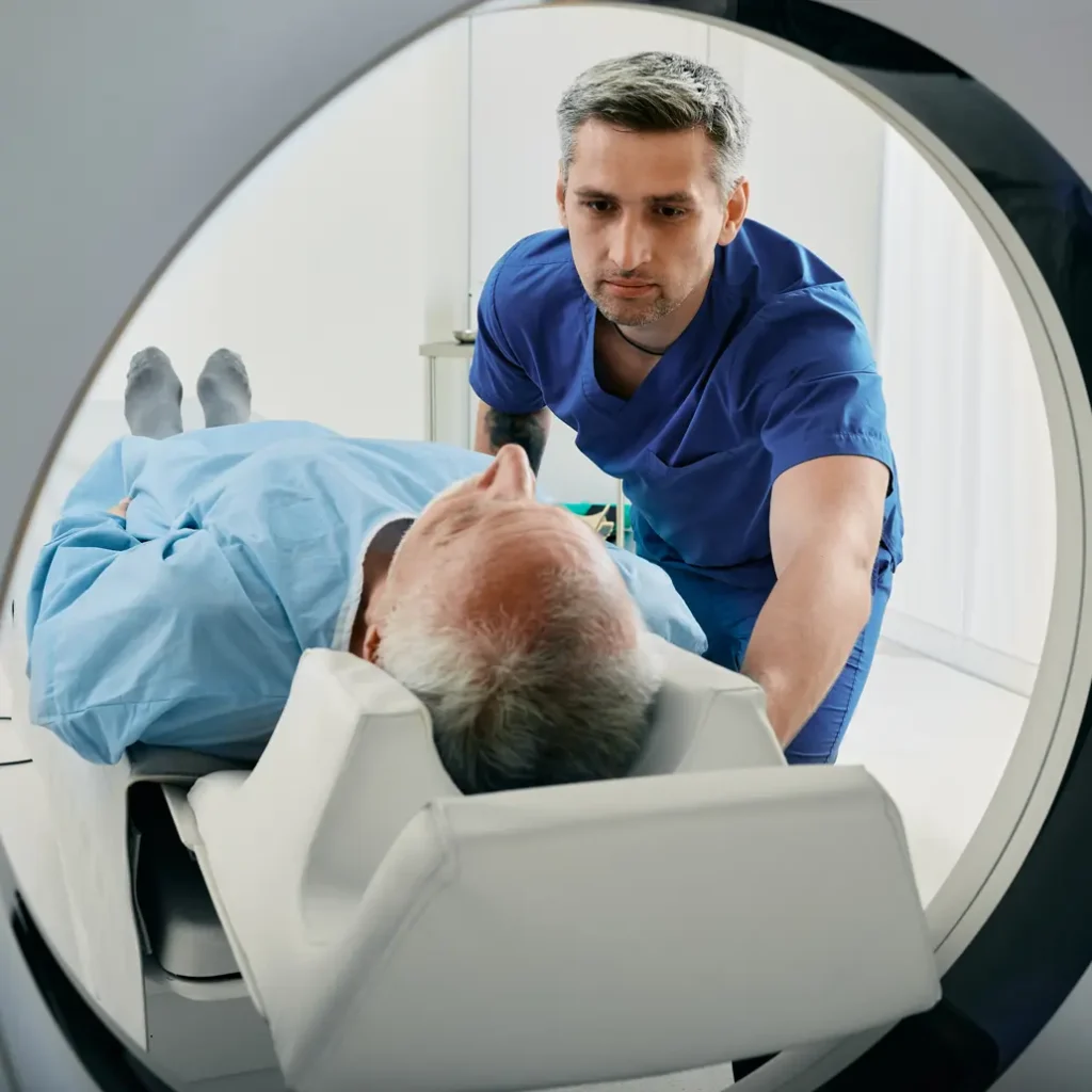 photo of a medical professional assisting an older male patient as he is entering a CT scanner