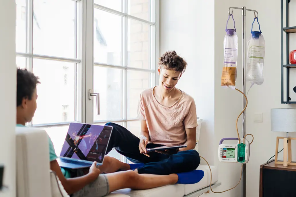 photo of two patients in a treatment center looking at their laptop and tablet devices while one is hooked up to a feeding pump